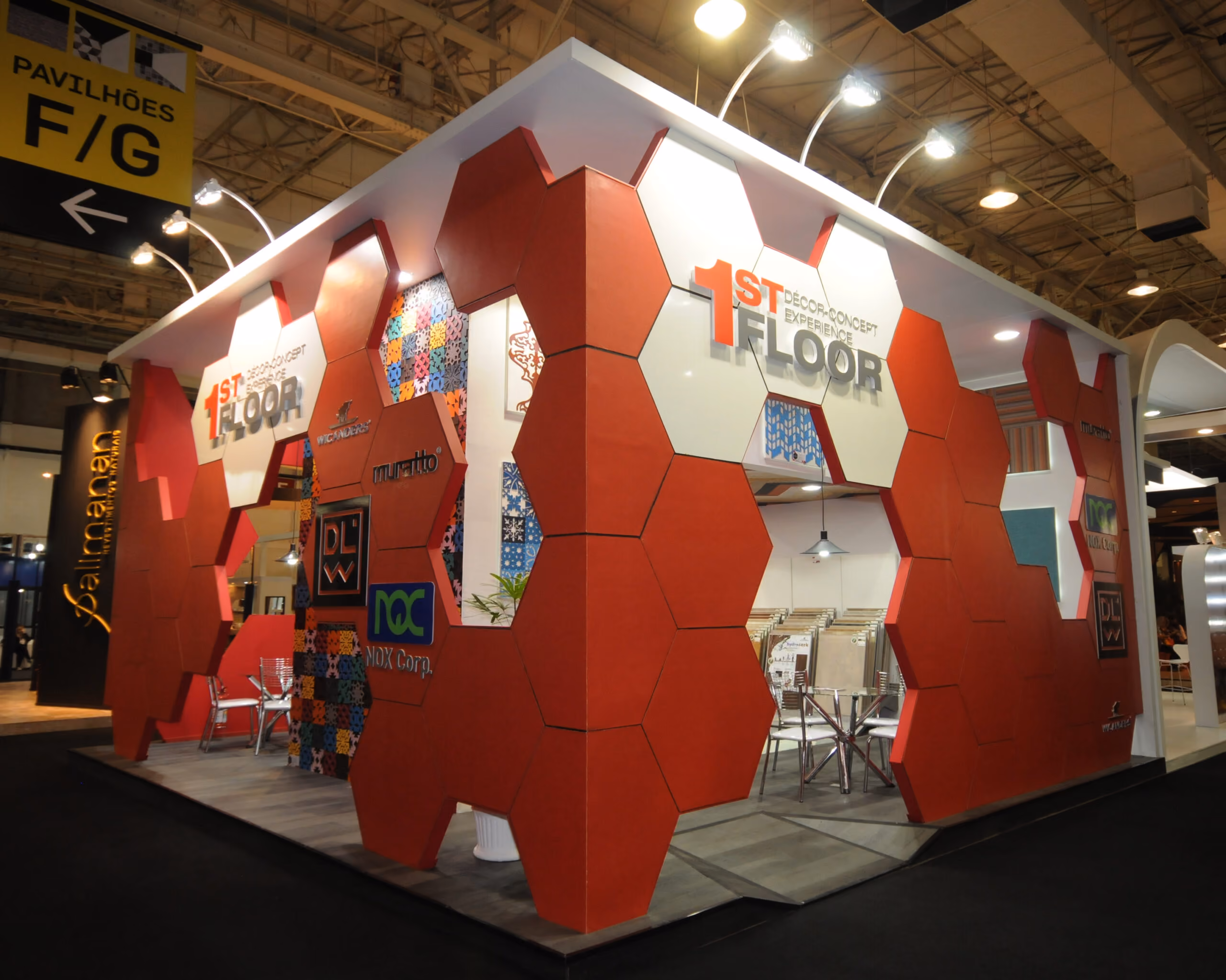 Estande com painéis vermelhos hexagonais exibindo o texto '1st Floor' em um espaço de exposição.